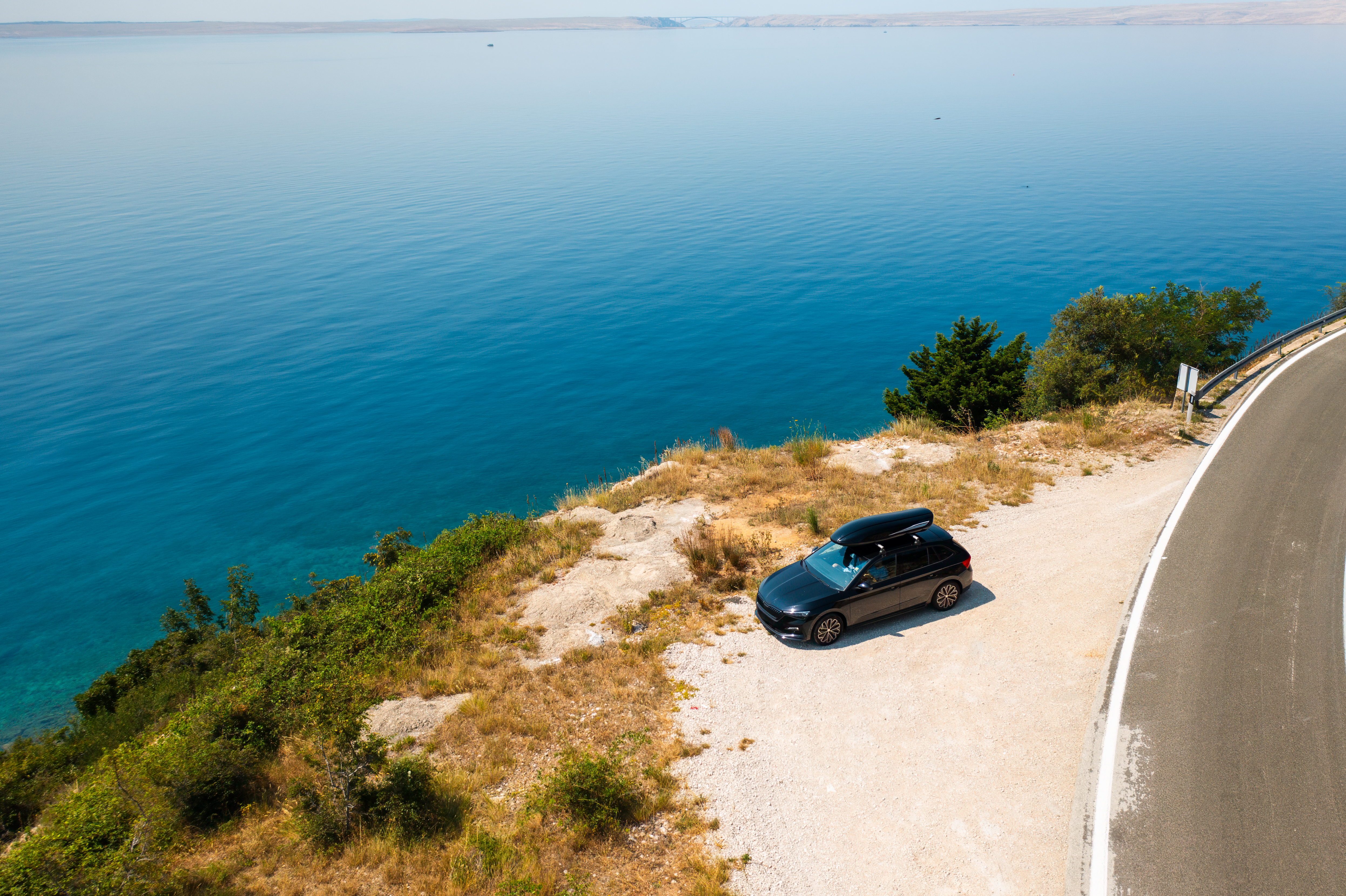 car-with-roof-box-parked-near-scenic-cliffside-road-overlooking-vast-azure-sea